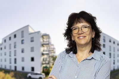 Eine Mitarbeiterin vor zwei Gebäuden.